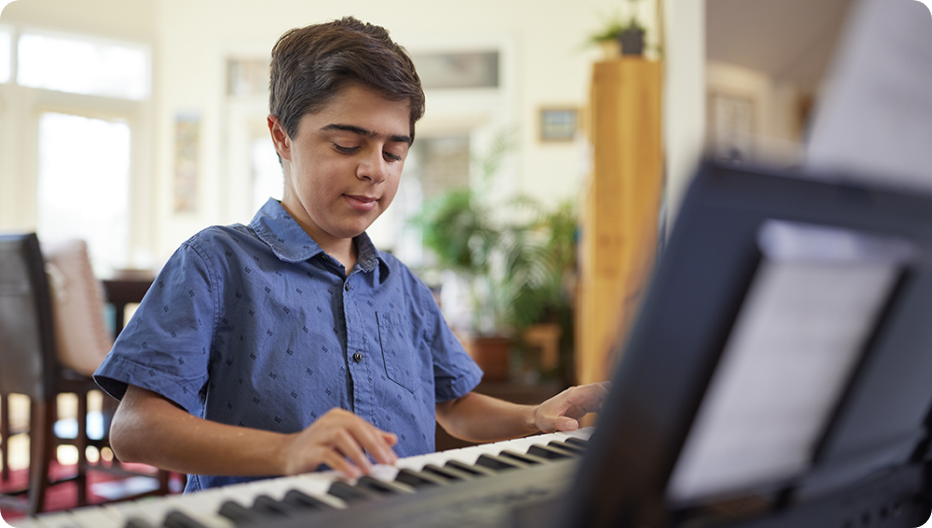 Teen child, a VILTEPSO patient, in a blue shirt focused on playing a keyboard piano indoors.